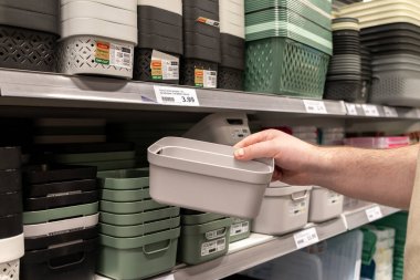 Poznan, Polonya - 30 Nisan 2025: Ev kullanımı için organizasyon ürünleri satın alma eylemini temsil eden çeşitli sepetlerle dolu bir mağaza rafından plastik bir konteynırı tutan bir elin yakın görüntüsü