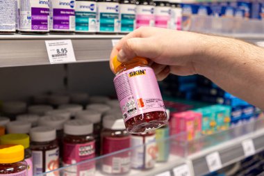 Poznan, Polonya - 30 Nisan 2025: Alışveriş yapan kişi, bir eczane koridorunda cilt sağlığı ve gıdalar için tasarlanmış bir vitamin ürünü seçiyor.