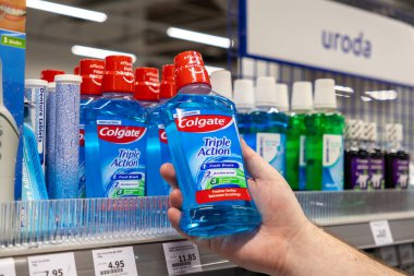 Poznan, Polonya - 30 Nisan 2025: Colgate Üçlü Eylem ağız yıkama ürünü şişesini tutan kişinin eli, bir mağaza vitrininde tüketicilerin ağız temizliği seçimini gösteriyor