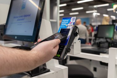 Poznan, Polonya - 30 Nisan 2025: Modern alışveriş kolaylığını gösteren, ışıl ışıl aydınlatılmış bir perakende mağazasındaki otomatik kontrol istasyonunda akıllı telefon kullanan bir müşteriye yakın çekim