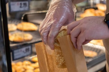 Açık plastik eldiveni sıhhatli bir şekilde kapatıyoruz. Fırın vitrinine taze pişmiş ekmek rulosu koyuyoruz. Hazır yemek siparişi için yiyecek güvenliğini gösteriyor.