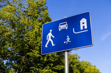 Yaya, araç, çocuk oyunu ve ev için beyaz sembollü mavi renkli ikamet bölgesi trafik levhası yayaların ve çocukların güvenliğini belirten paylaşılan alanı simgeliyor.