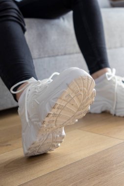 Ahşap bir zeminde giyilen, modern şehir modasını ve bireysel yaşam tarzını temsil eden, rahat beyaz topaklı spor ayakkabılarının ayrıntılı görüntüsü