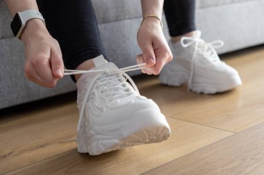 Modern tıknaz spor ayakkabılarının beyaz ayakkabı bağcıklarını sıkılaştıran ellerinizi kapatın, rahat ve şık ayakkabıları gündelik kıyafetlere hazırlama rutinini temsil ediyor.