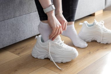 Kapalı mekanlarda kilolu spor ayakkabıları giyip, rahat ve destekleyici spor ayakkabıları hazırlamanın rutinini anlatan ellerin detaylı görüntüsü.