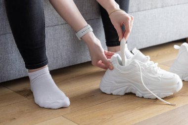 Ellerinizi kapayın, beyaz ayakkabı ağacını modern spor ayakkabılarına yerleştirin, ahşap zemin üzerinde, rahat spor ayakkabılarını korumak için kişisel rutininizi temsil ediyor.