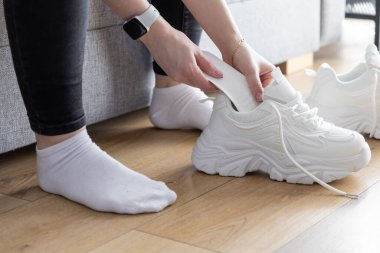 Beyaz ayakkabı şekillendiricisini modern spor ayakkabıların içine yerleştirerek ahşap zemine yerleştiren ellerin detaylı görüntüsü, konforlu spor malzemelerinin korunması için kişisel rutini gösteriyor.