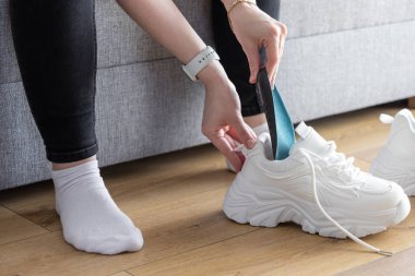 Spor ayakkabılarını kişiselleştirmek için, ahşap zemindeki tıknaz spor ayakkabılarının içine mavi taban yerleştiren eller.