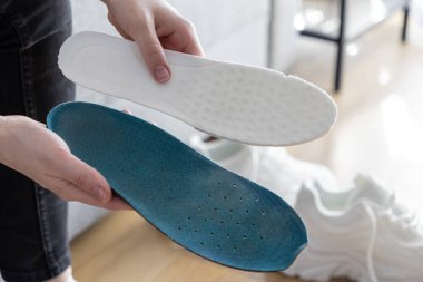 İçerideki mavi ve beyaz ortopedik tabanları sunan elleri kapatın, rahat ve destekleyici spor ayakkabıları yerleştirme seçeneklerini temsil edin