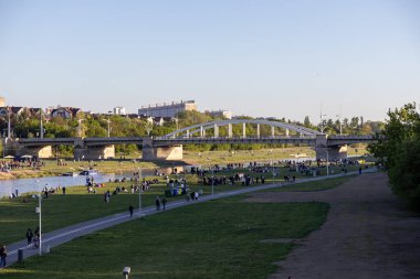 Poznan, Polonya - 25 Nisan 2025: Warta Nehri şehir parkı ve köprü kenarındaki çimenli bankanın keyfini çıkaran birçok insan