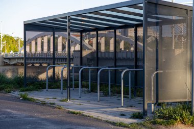Şehir köprüsü yakınlarında boş metal rafları olan modern cam panelli bisiklet sığınağı, çevre dostu banliyö, şehir altyapısı ve toplu taşıma tesislerini sembolize ediyor