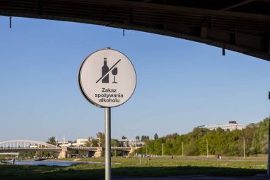 Lehçe alkol kullanımının yasak olduğuna işaret eden Lehçe alkol tüketimi metninde üstü çizilmiş şişe simgesi ve metin içeren yuvarlak beyaz halka açık tabela