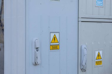 Dışarıdaki gri elektrik dolabında uyarı işareti simgesi ve metin var. Lehçe elektrik güvenliğini destekleyen elektrik aygıtı metnine dokunmayın.