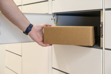 Kahverengi bir karton kutuyu açmak için beyaz bir dolap açan eller, otomatik paket koleksiyonunun modern verimliliğini gösteriyor.