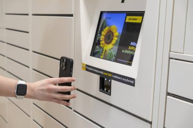 Poznan, Polonya - 2 Mayıs 2025: Bir InPost paket dolabındaki QR kodunu taramak için akıllı telefon tutan bir el, paket alımını düzenliyor