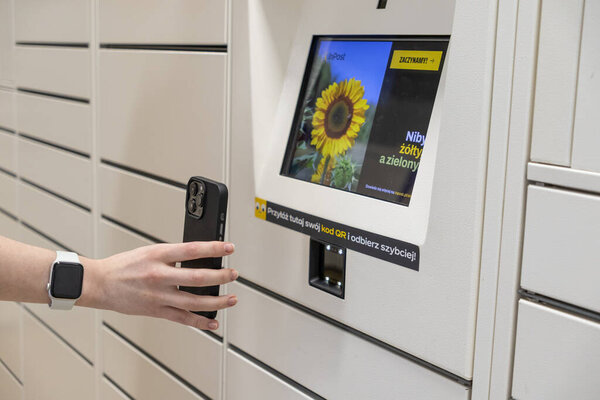 Poznan, Poland - May 2, 2025: A hand holding a smartphone is positioned to scan a QR code on an InPost parcel locker, streamlining package retrieval