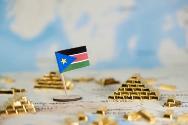 Küçük bir Güney Sudan bayrağı, ülkenin ekonomik potansiyelini, doğal kaynaklarını ve küresel yatırımı sembolize eden birçok minyatür altın külçeli bir dünya haritasında yer alıyor.