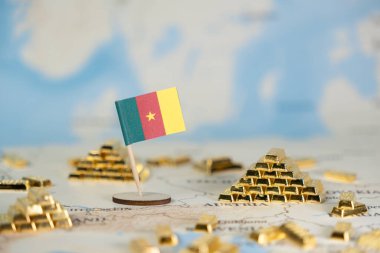 Küçük bir Kamerun ulusal bayrağı, minyatür altın külçeleri, ekonomik kalkınmayı, küresel yatırımı ve değerli varlıkları sembolize eden bir jeopolitik harita üzerinde duruyor.