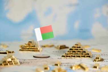 Madagaskar bayrağı bir dünya haritasında, ülkenin ekonomik potansiyelini, doğal kaynaklarını, küresel yatırımı ve tasarım için bolca kopya alanını yansıtan altın külçeleriyle çevrili.