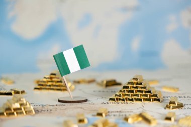 Minyatür Nijerya bayrağı ve altın külçeleri, ülkenin ekonomik potansiyelini, mali yatırımlarını ve emtia piyasası statüsünü temsil eden bulanık bir dünya haritasına yerleştirilmiştir.