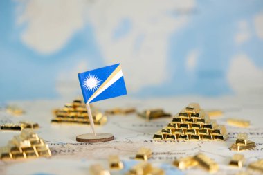 Marshall Adaları 'nın minyatür bir bayrağı, dünya haritasındaki parıldayan altın külçeleri arasında ulusal varlıkları, finansal güvenliği ve küresel ekonomik gücü kopya alanı ile temsil ediyor.