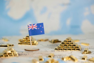 Dünya haritasında parlayan altın çubuk piramitlerin arasına dikilmiş küçük bir Yeni Zelanda bayrağının yakın plan görüntüsü, ekonomik istikrar ve küresel ticaret