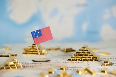 Bulanık bir dünya haritasına yerleştirilmiş küçük bir Samoa bayrağına yakın plan, dağınık minyatür altın külçeler, bir ülkenin finansal durumunu, küresel ticaretini ve ekonomik refahını sembolize ediyor.