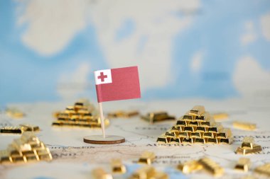 Tongan bayrağının yakın plan görüntüsü ulusal kaynak yönetimi ve finansal refahı temsil eden detaylı bir dünya haritasında birden fazla altın külçesinin arasına gururla yerleştirilmiştir.