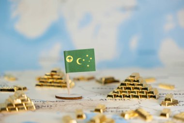 Canlı bir Cocos (Keeling) Adaları bayrağı, ulusal varlıkları, ekonomik istikrarı ve kazançlı küresel ticareti gösteren bir dünya haritasında dağınık altın külçeleri arasında yerini alıyor.