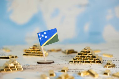 Minyatür Solomon Adaları bayrağı, küresel ekonomiyi, değerli yatırımı ve kaynak zenginliğini temsil eden birçok altın külçesiyle çevrili detaylı bir dünya haritasında yer almaktadır.