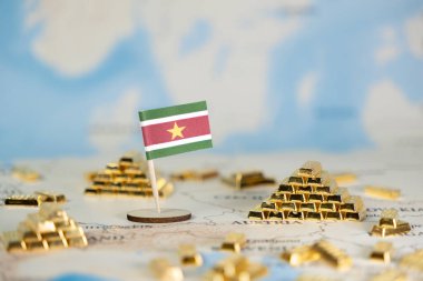 Küresel haritada küçük Surinam bayrağının ve parıldayan altın külçelerinin yakın çekimi, ulusal refahı, finansal varlıkları ve jeopolitik önemi temsil eder.