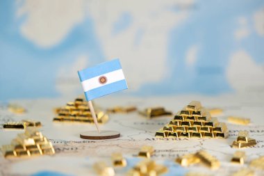 Arjantin bayraklı bir dünya haritasının arka planında, ulusal rezervleri, yatırımları ve uluslararası finans stratejisini gösteren bir minyatürü çevreleyen minyatür altın külçeler