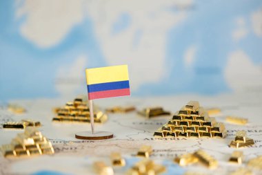 Bulanık bir dünya haritasına dağılmış Kolombiya bayrak iğnesi ve minyatür altın külçelerin üst görüntüsü ulusal kaynak zenginliğini, küresel finans piyasalarını ve ekonomik gücü temsil ediyor.