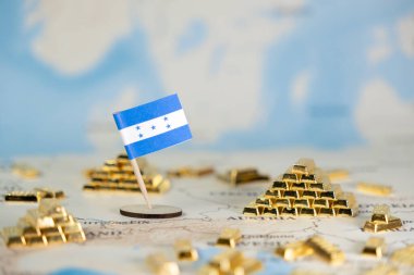 Küçük bir Honduras bayrağı, ulusal zenginlik, ekonomik istikrar, küresel finans ve uluslararası ticareti gösteren altın külçeleri arasında bir dünya haritasında duruyor.