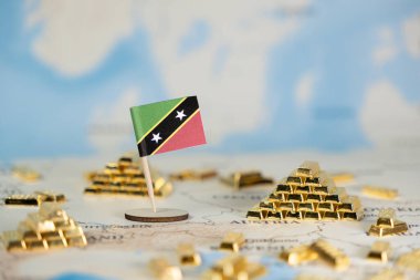 Minyatür altın külçelerle çevrili bir dünya haritasında canlı Saint Kitts ve Nevis bayrağı, mavi arkaplanlı ulusal mali gücü ve küresel yatırımı vurguluyor