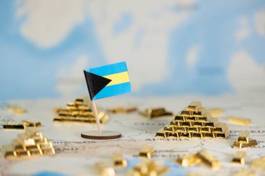 Bahamalar bayrağı, küresel finans, açık denizaşırı zenginlik ve ekonomik istikrarı açıkça sembolize eden birçok altın külçesiyle çevrili bir dünya haritasında sergilenmektedir.