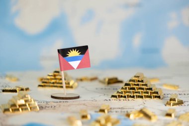 Antigua ve Barbuda 'nın küçük bir bayrağı, dünya haritasında minyatür altın külçeleri arasına, uluslararası finans, pazar eğilimleri ve boş alan ile ekonomik istikrarı gösteren bir bayrak yerleştirilmiştir.