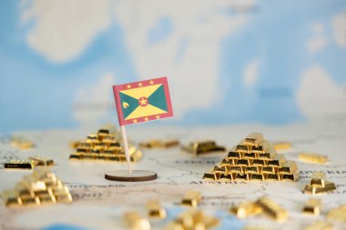 Bir Grenada bayrağı, küresel finans stratejisi, kaynak yönetimi ve ulusal ekonomik büyüme potansiyelini temsil eden minyatür altın külçeleriyle birlikte bulanık bir dünya haritasında yer alıyor.