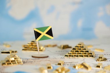 Bir dünya haritasında küçük bir Jamaika bayrağı yer alıyor, birçok pırıl pırıl altın külçelerle çevrili, ulusal zenginliği, ekonomik büyümeyi, küresel finans ve yatırımı vurguluyor.