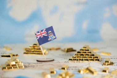 Bir dünya haritasında Cayman Adaları bayrağının yukarıdan aşağı görüntüsü, minyatür altın külçeleri, off-shore bankacılık, küresel yatırım ve zenginlik birikimini sembolize ediyor