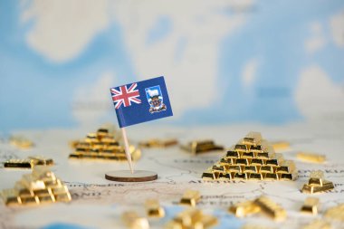 Falkland Adaları 'nın minyatür bir bayrağı, detaylı bir dünya haritasında, ekonomik fırsatları ve toprak taleplerini temsil eden dağınık altın külçeleriyle belirgin bir şekilde sergilenmektedir.