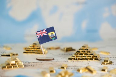 Haritadaki altın külçeleriyle çevrili minyatür Saint Helena bayrağı, küresel ticarette İngiltere 'nin denizaşırı bölgelerinde finansal değeri, deniz mirası ve ekonomik beklentilerini temsil ediyor.