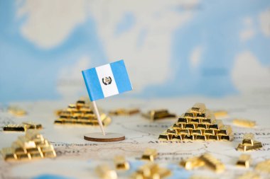 Ulusal refah, küresel ticaret ve kaynak yönetimini temsil eden bulanık bir dünya haritasına küçük bir Guatemala bayrağı ve sayısız parlak altın çubuk minyatürü yerleştirildi.