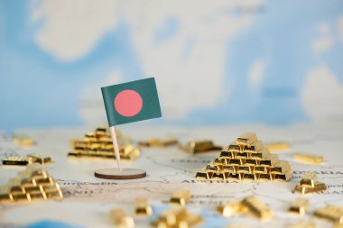 Ulusal finans stratejisi ve küresel ekonomik kalkınmayı temsil eden ayrıntılı bir dünya haritasında, sayısız dağınık minyatür altın külçe destesiyle birlikte küçük bir Bangladeş bayrağı yer alıyor.