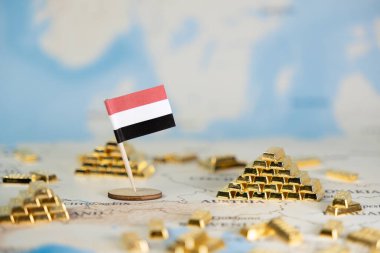 Yemen 'in minyatür bayrağı, uluslararası yatırım için ulusal ekonomik kaynakları ve küresel emtia değerini gösteren bulanık bir dünya haritasına yerleştirilmiş parlak altın külçeleriyle sergileniyor.