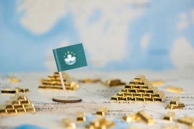 Ulusal ekonomik refah, zenginlik ve küresel yatırım potansiyelini ön plana çıkaran sayısız altın külçeli bir dünya haritasında minyatür bir Macau bayrağının ayrıntılı görüntüsü