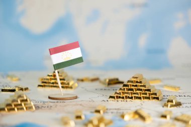 Dünya haritasında yer alan minyatür Tacikistan bayrağı ve altın külçeleri ulusal zenginliği, küresel yatırımı ve geniş bir kopya alanına sahip mali stratejiyi gösteriyor