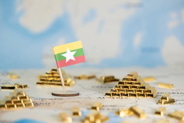 Ülkenin ekonomik gücünü, kaynak potansiyelini ve uluslararası finans fırsatlarını simgeleyen pek çok parlak altın külçeli haritanın üzerinde duran küçük bir Myanmar bayrağının yakın çekimi
