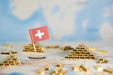 Dünya haritasındaki küçük İsviçre bayrak iğnesi, finansal gücü, refahı, ekonomik istikrarı ve güvenilir küresel yatırımı sembolize eden minyatür altın külçelerle çevrili.