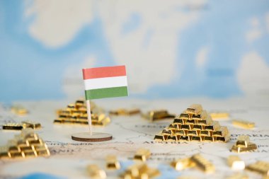 Minyatür Macar bayrağı, ülkenin ekonomik gücünü, rezervlerini ve yatırım potansiyelini vurgulayan sayısız altın külçesiyle ayrıntılı bir dünya haritasında gururla duruyor.